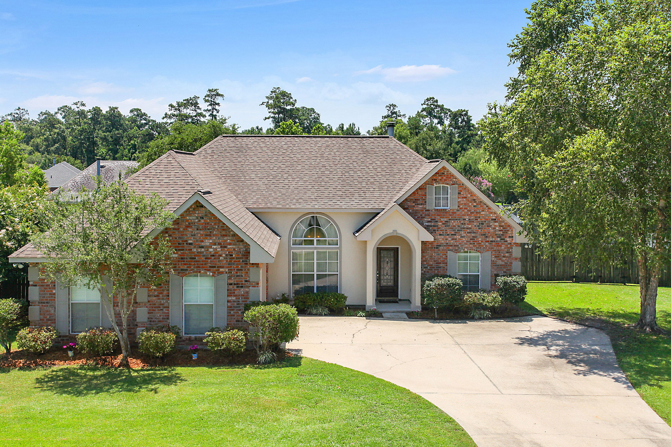 A charming brick house with a curved driveway and well-kept lawn.
