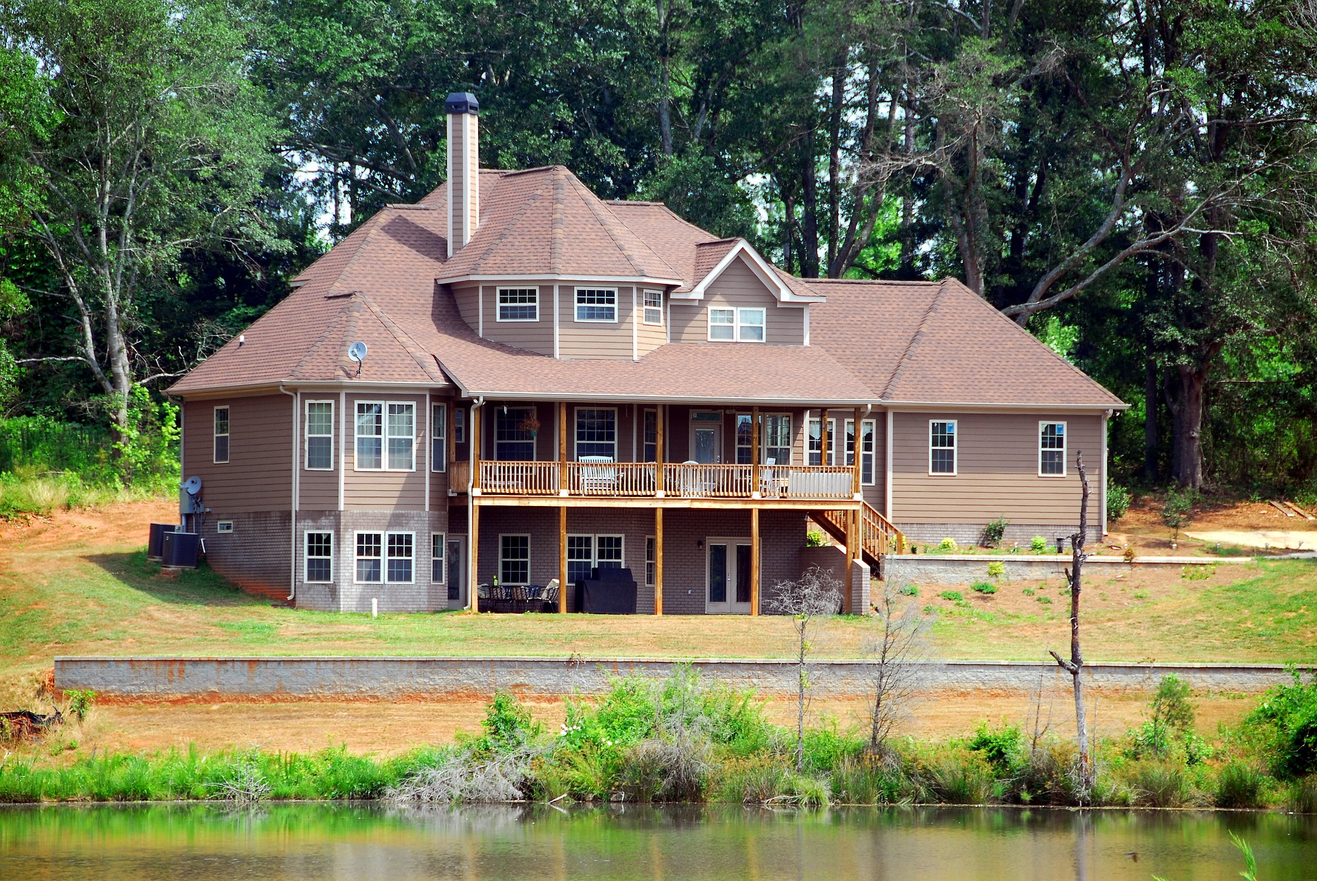 Large lakeside house surrounded by trees with a wooden deck.