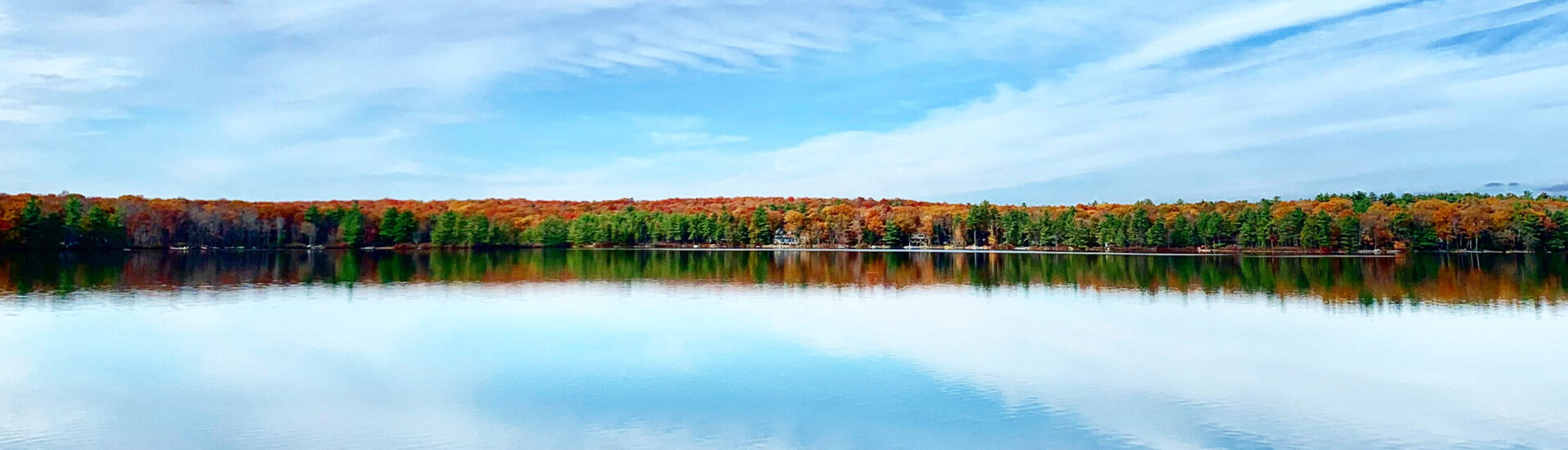 A calm lake reflecting autumn trees under a clear sky.